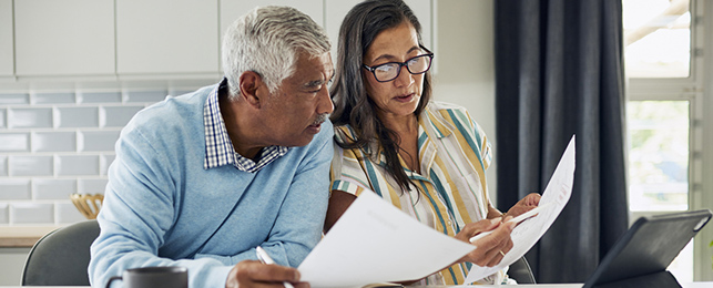 An older couple is sitting at their kitchen table reviewing documents