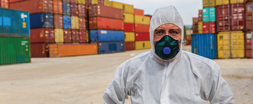 man in hazmat suit standing in front of shipping containers